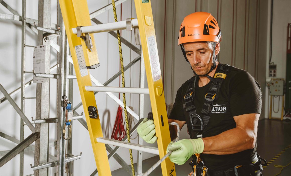 Técnico con equipo de protección y arnés trabajando con escalera en curso de seguridad en altura de Altiur Formación.