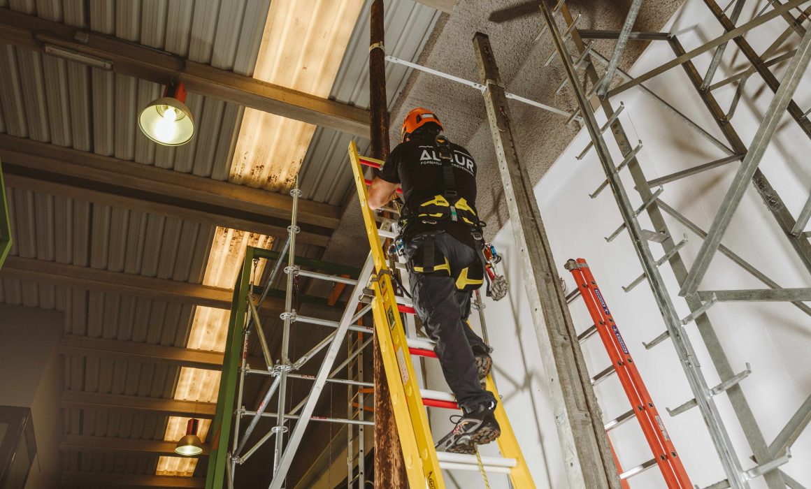 Trabajador con arnés subiendo por una escalera durante práctica de trabajos en altura en curso de seguridad laboral de Altiur Formación.
